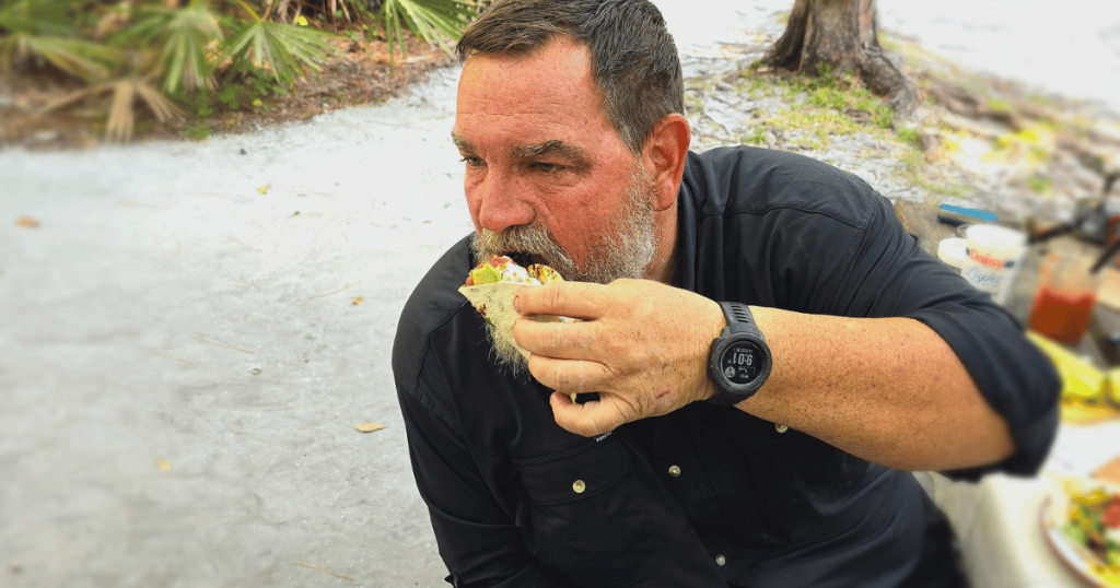 MAN EATING A BREAKFAST TACO AT CAMP