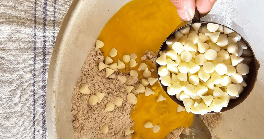 PUMPKIN WHITE CHOCOLATE SCONES WITH BOURBON MAPLE GLAZE DUMPING WHITE CHOCOLATE CHIPS INTO BOWL