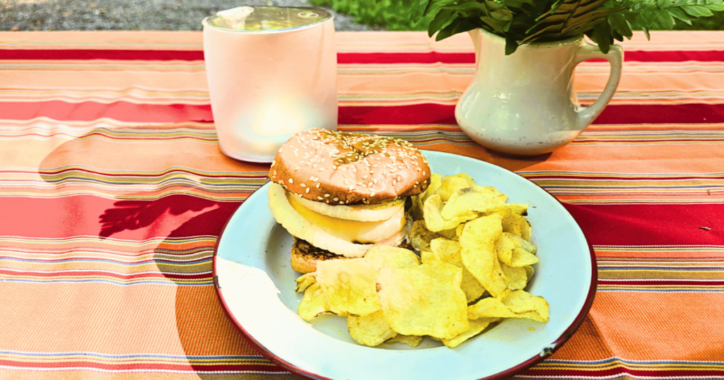 QUICK & EASY CAMPING SIDE DISH IDEAS FOR OUTDOOR ADVENTURES hamburger and chips on a plate on a picnic table
