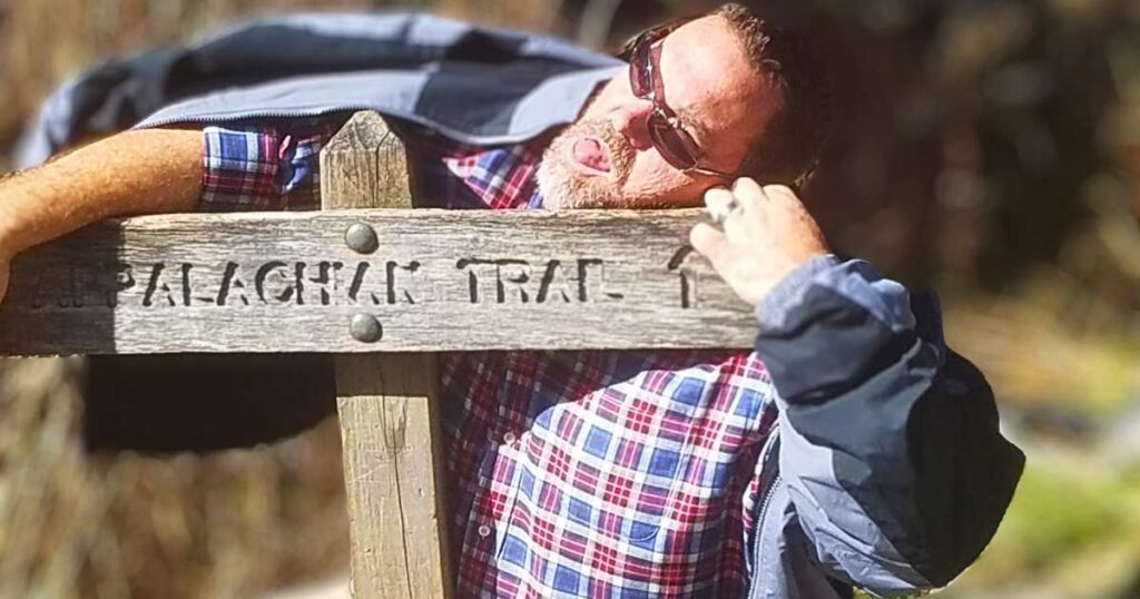 BEGINNER'S GUIDE TO CAMPING THIS IS AN IMAGE OF A GUY HUGGING A TRAIL SIGN