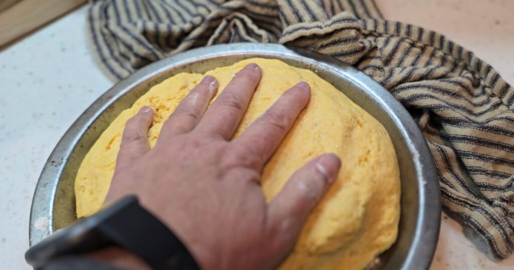 THIS IS AN IMAGE OF A HAND PUSHING DOWN BREAD DOUGH IN A PIE PAN,