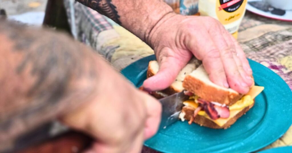 Easy Camping Breakfast Sandwich THIS IS AN IMAGE OF A MAN CUTTING AN EASY CAMPING BREAKFAST SANDWICH