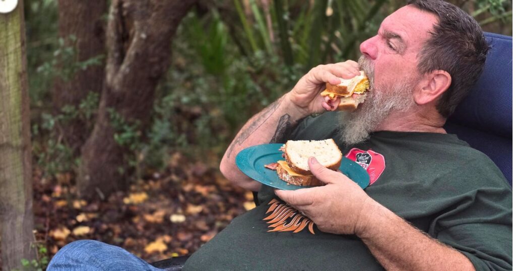 Easy Camping Breakfast Sandwich THIS IS AN IMAGE OF A MAN EATING AN EASY CAMPING BREAKFAST SANDWICH