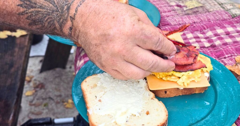 THIS IS AN IMAGE OF A MAN ASSEMBLING A EASY CAMPING BREAKFAST SANDWICH