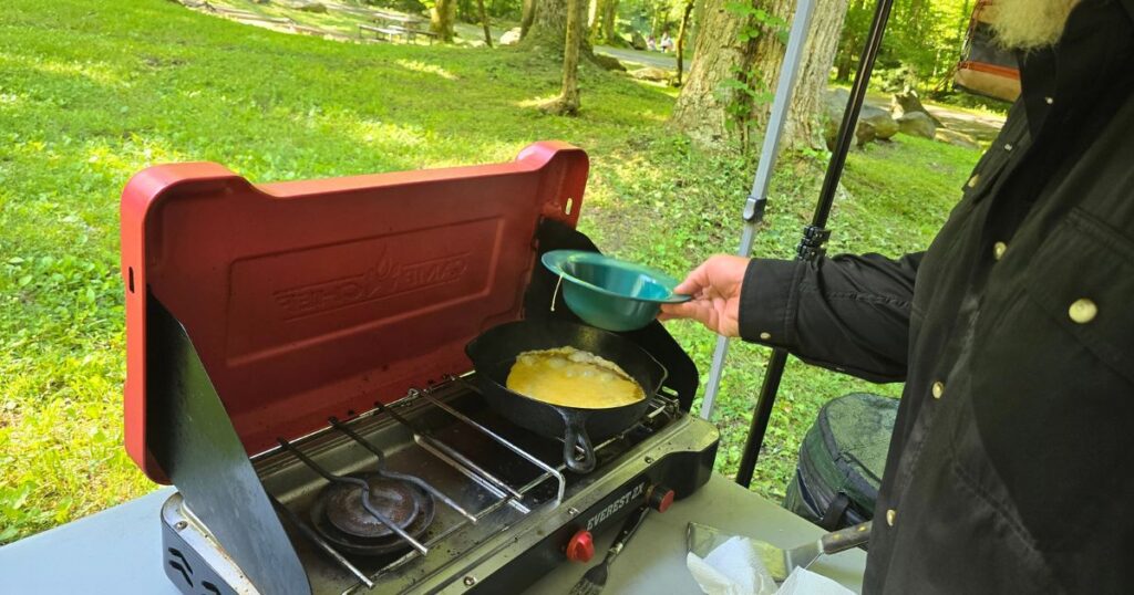 THE BEST CAR CAMPING PORTABLE KITCHEN AND SETUP THIS IS AN IMAGE OF A MAN COOKING ON THE CAMP CHEFT EVEREST PORTABLE CAMP STOVE