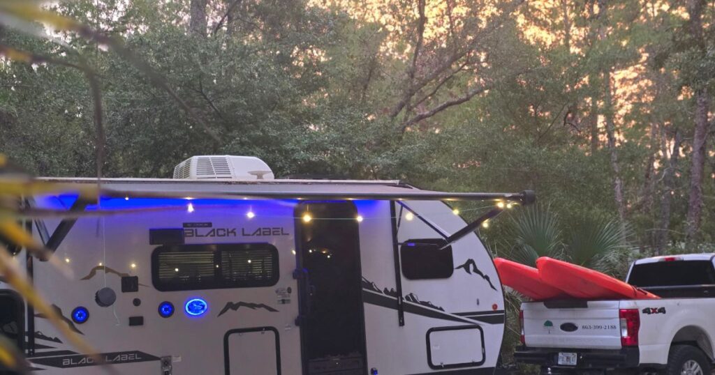 Remote camping trailer with kayak on truck in forest during sunset.