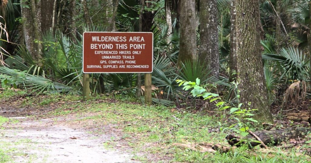 Wilderness area beyond this point sign in a lush jungle setting with trees and tropical plants.