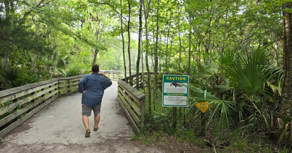 Upland trail leading to nature reserve with warning signs about wildlife and crocodiles, surrounded by lush green forest.