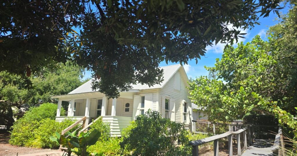 Charming white cottage surrounded by lush greenery and mature trees in a tranquil outdoor setting.