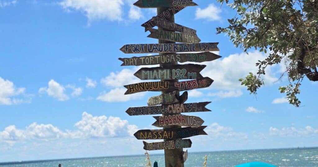 Colorful travel signpost pointing to various destinations by the beach.