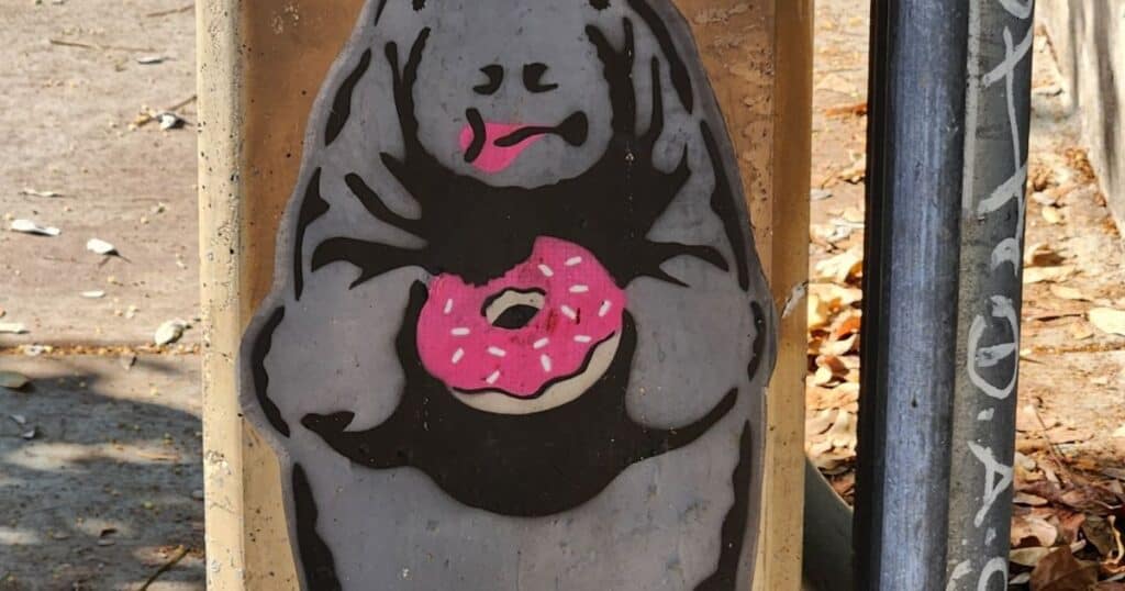 Colorful street art of a cute hipster Sasquatch holding a pink donut, outdoor urban mural, quirky Bigfoot illustration.